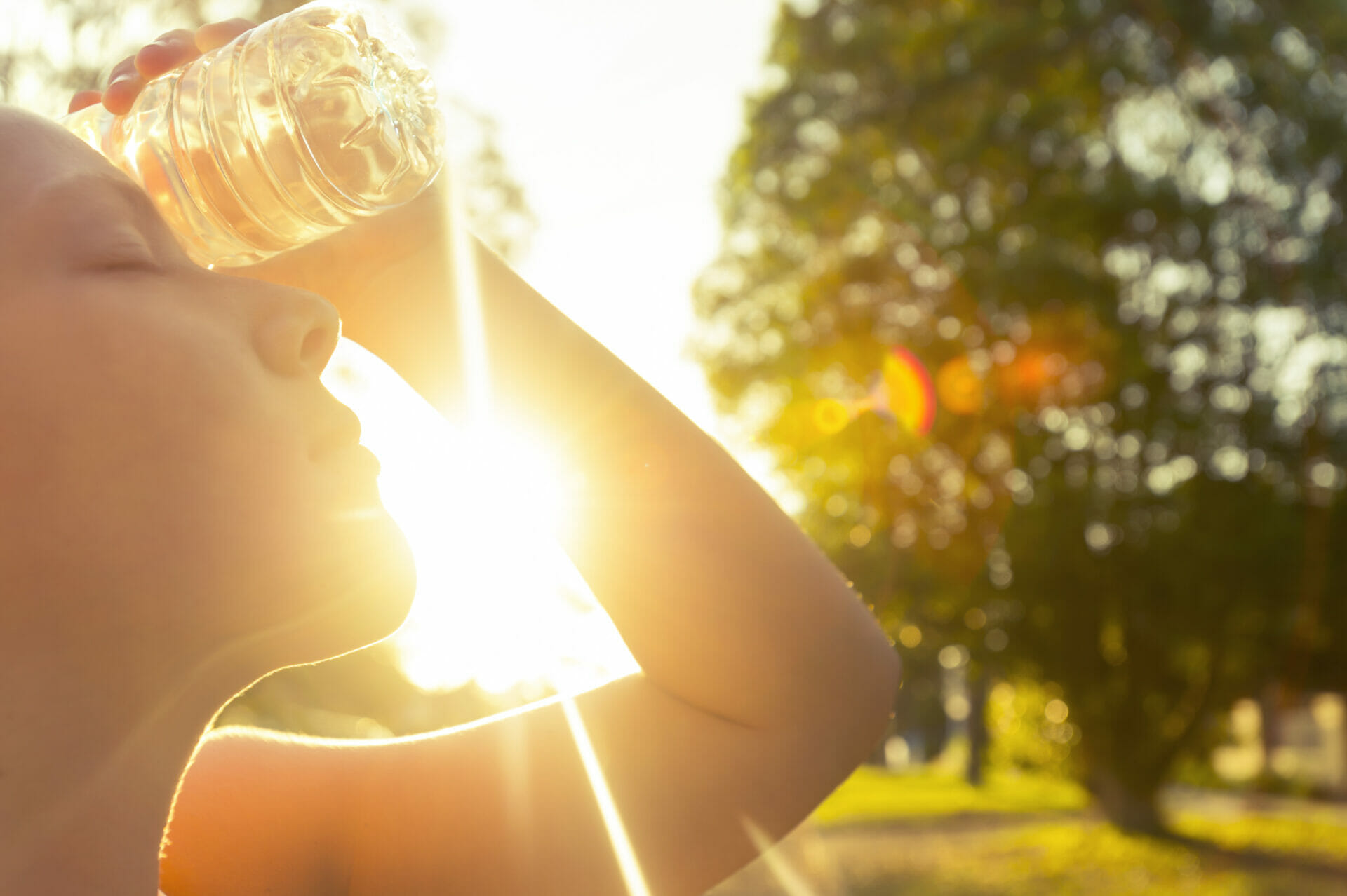 Person cools down with water bottle on their face, in heat. Istock image.