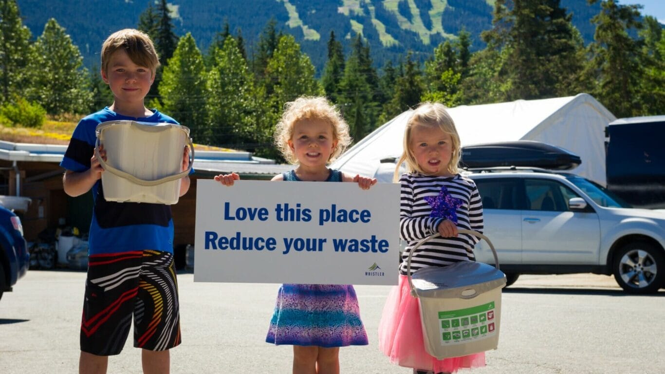 Children holding compost bins and a sign saying "Love this place; reduce your waste"