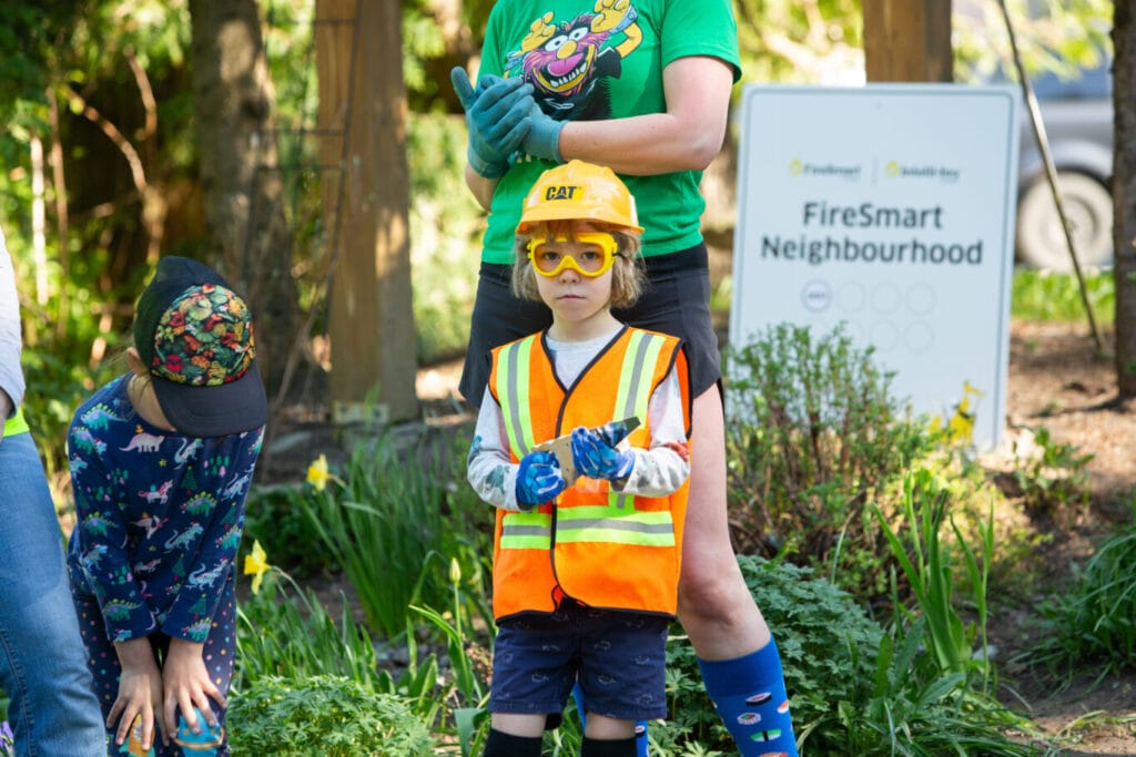 A young child in construction clothing helps FireSmart a neighbourhood