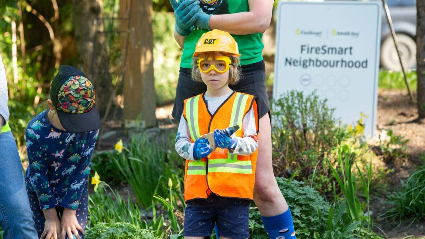 A young child in construction clothing helps FireSmart a neighbourhood